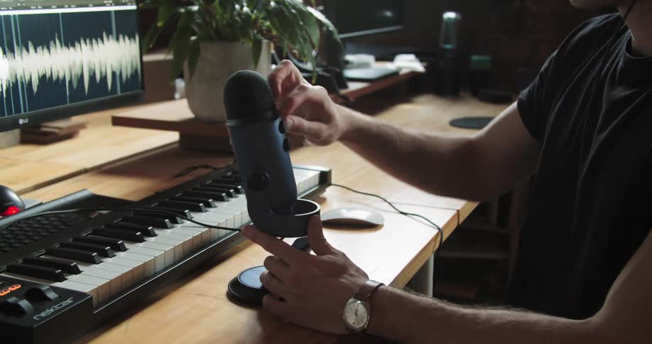 A man records music at a desk with a keyboard and microphone