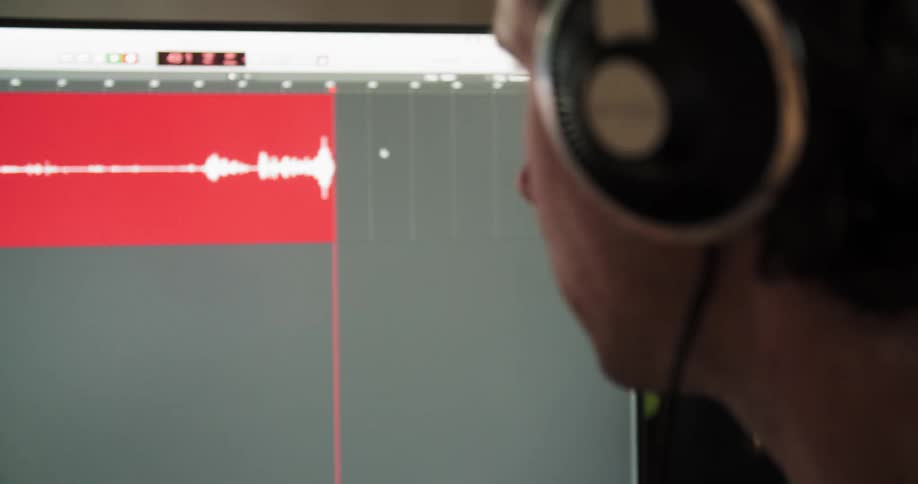 Man wearing headphones and sitting at the desk records his voice for the software on the display