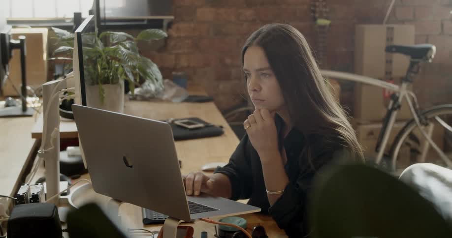 A woman sits in front of a laptop on a stand working