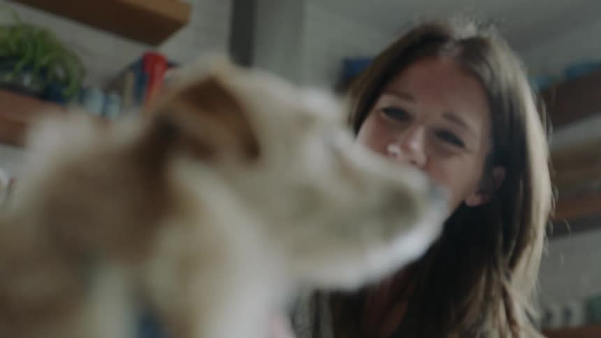 A woman pets her dog while in a kitchen