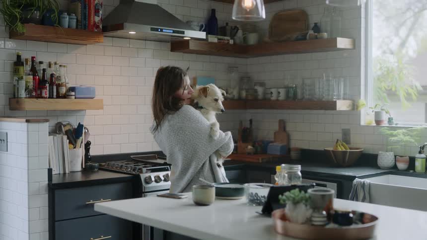 Woman holds a dog in her arms on kitchen in a house