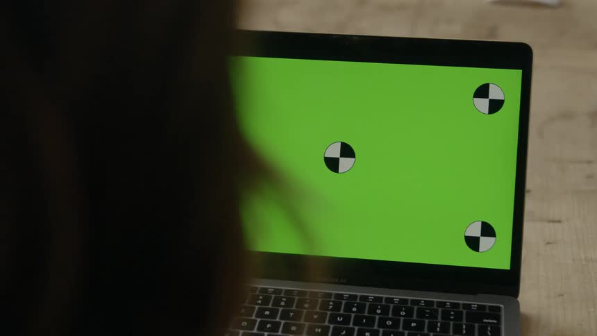 A woman sits talking in front of a laptop displaying a green screen with black and white circles on it