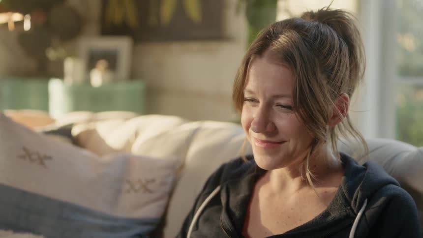 Woman sits on couch smiling while watching