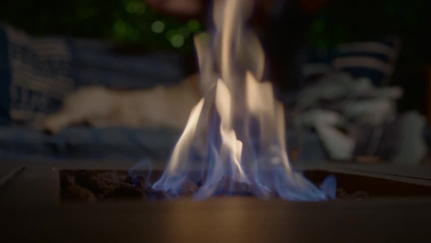 A person and dog sit on patio furniture next to a gas fire pit