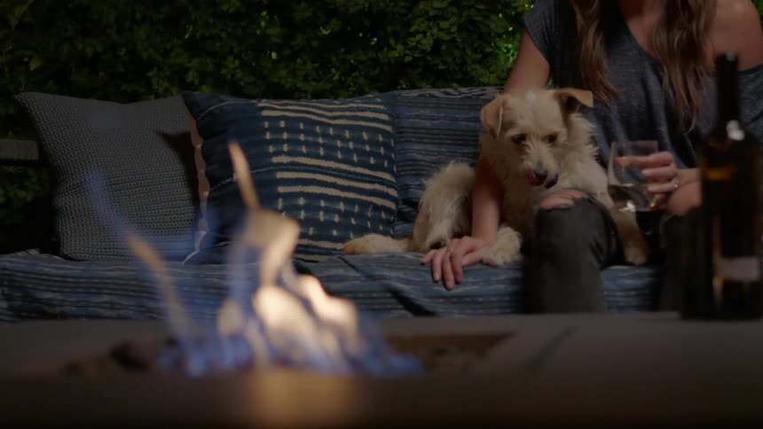 A woman sitting in an outside patio next to a dog and close to a fire pit