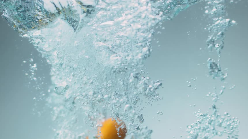 Several pieces of citrus fruit are dropped below the surface of crystal clear water