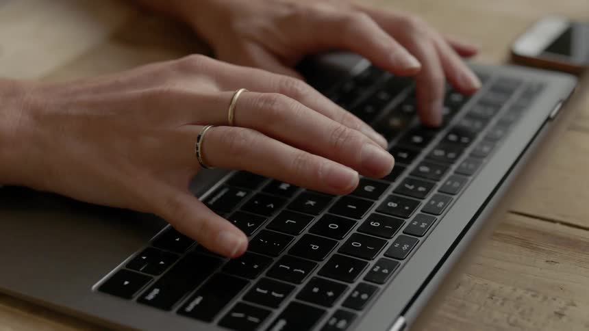 A womans hands typing on a keyboard