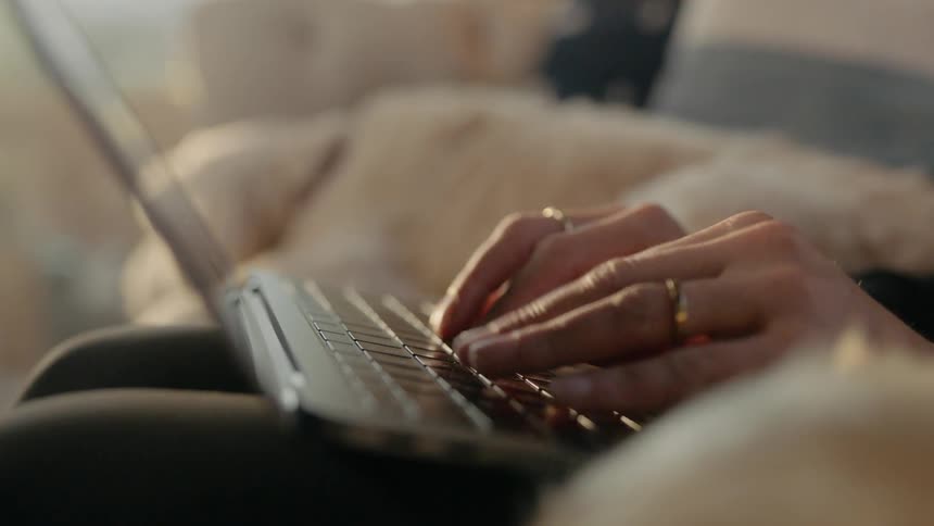 A woman types on a laptop while sitting on a sofa