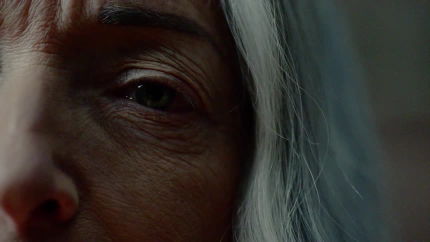 An elderly woman blinks her eye as a shadow passes before her