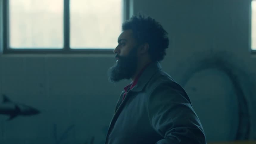 A man walks through a large empty room while wearing a jacket