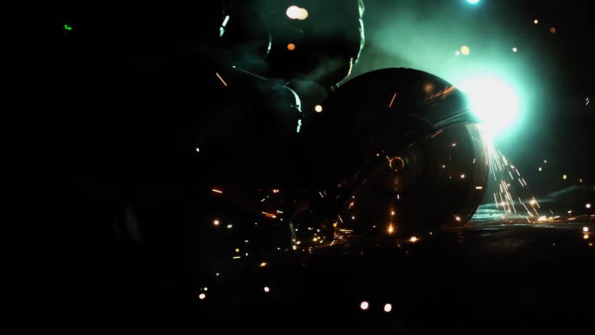 Electric metal cutting saw grinding a metal plate throwing sparks on dim lit room