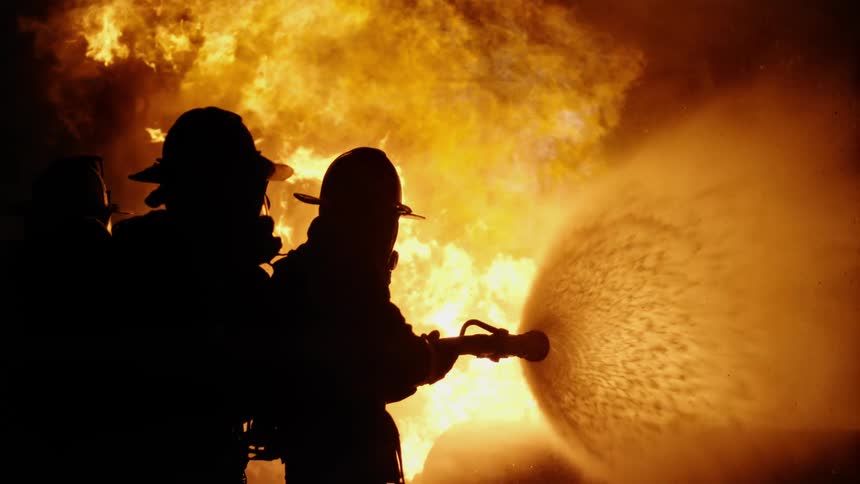 Firefighters point a hose at a large fire