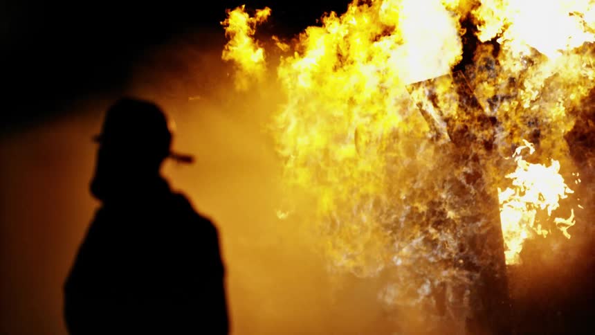 A firefighter stands in front of a house in flames