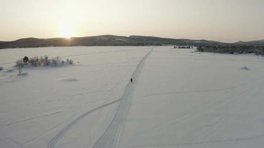 An aerial view of a person riding a bike across a snowy lake at sunrise