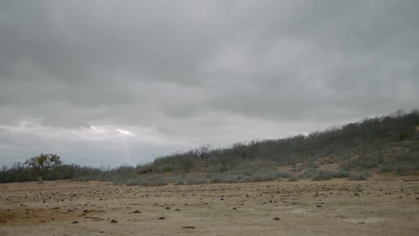 Clouds float above a dirt field and hill