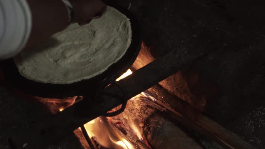 A person spread flat bread batter on a pan over an open flame