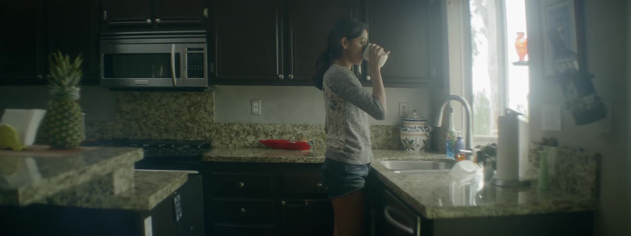 A woman drinks from a coffee cup standing in a kitchen
