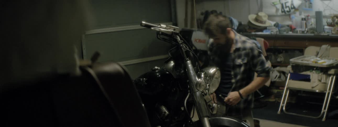 A man walks into his garage and sits down to work on his motorcycle