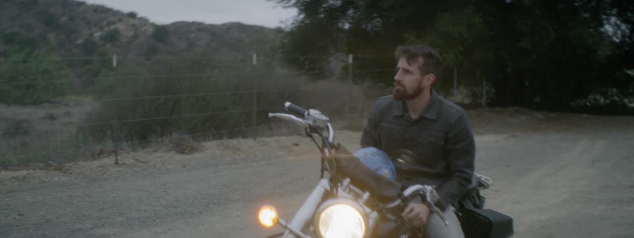 Man sits on a stopped motorcycle near the trees