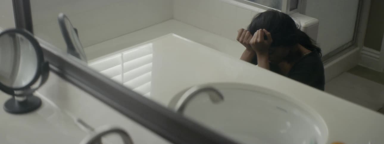 A sad woman sits on the floor of a bathroom with her head in her hands