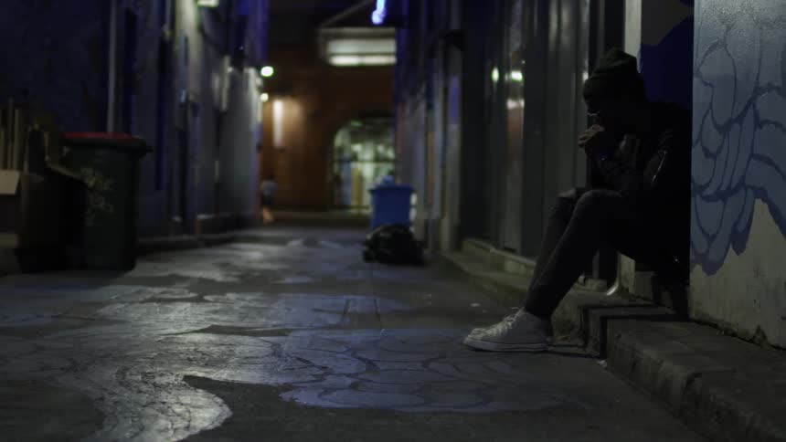 A man sits on a stoop in an empty alley at night