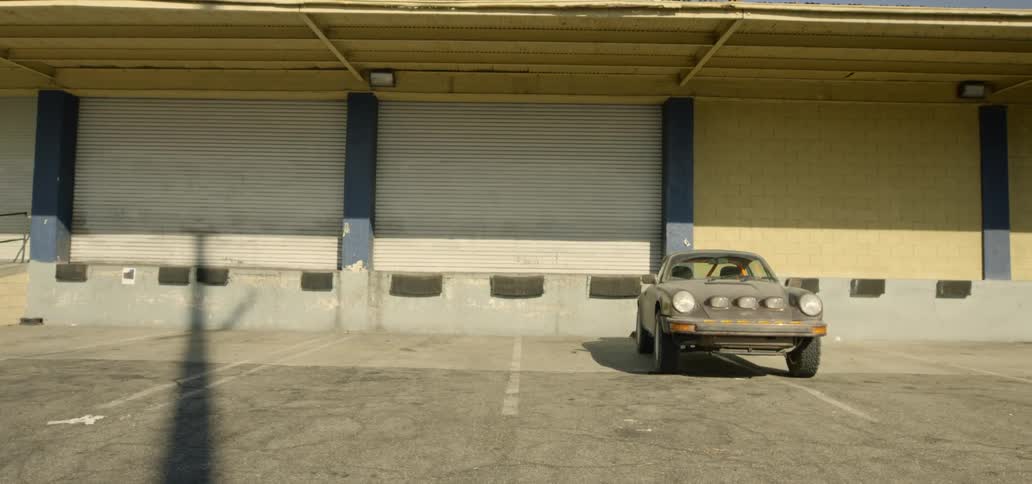 A vintage car sits outside of large commercial garage doors