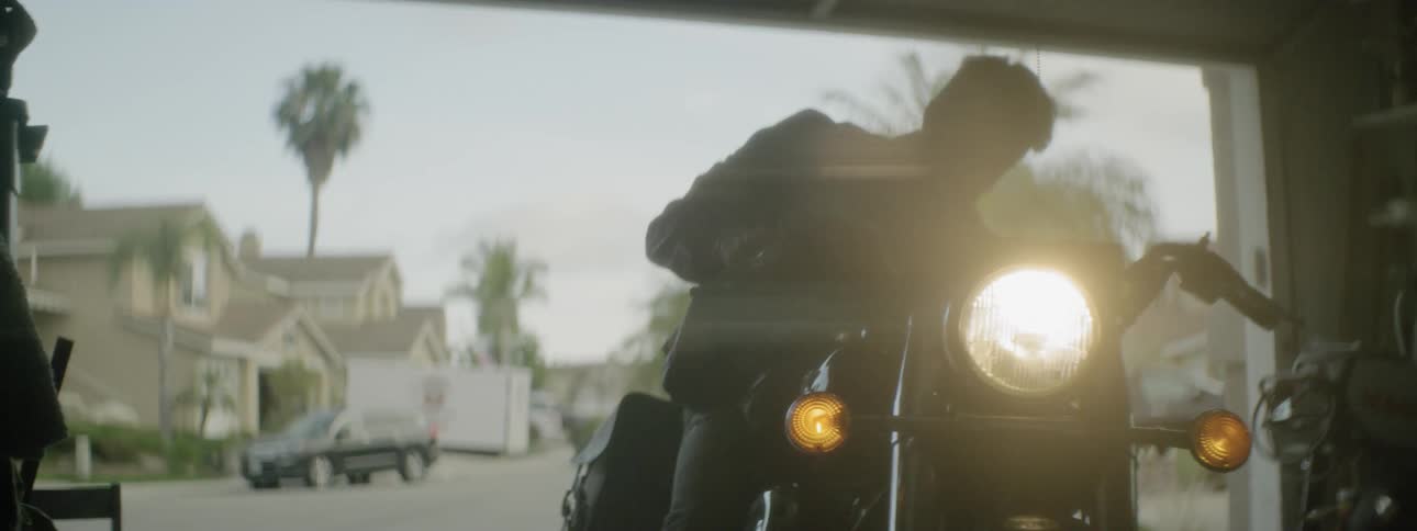 A man starts his motorcycle and puts his helmet on while in his garage with the door open