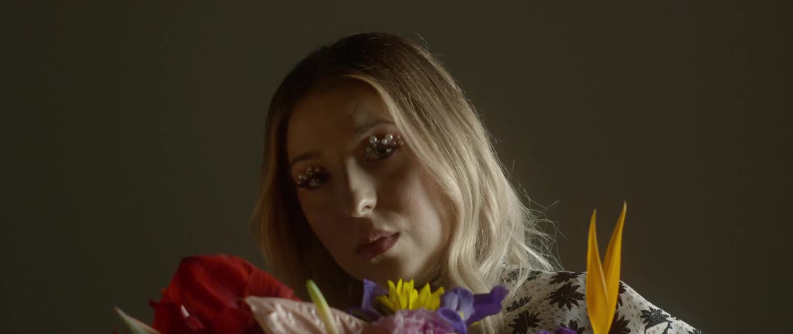 A woman with beads on her eyelids holds a bouquet of flowers in front of her face