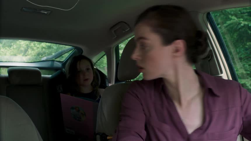 Woman with daughter in rear seat starts car and looks over shoulder to backup