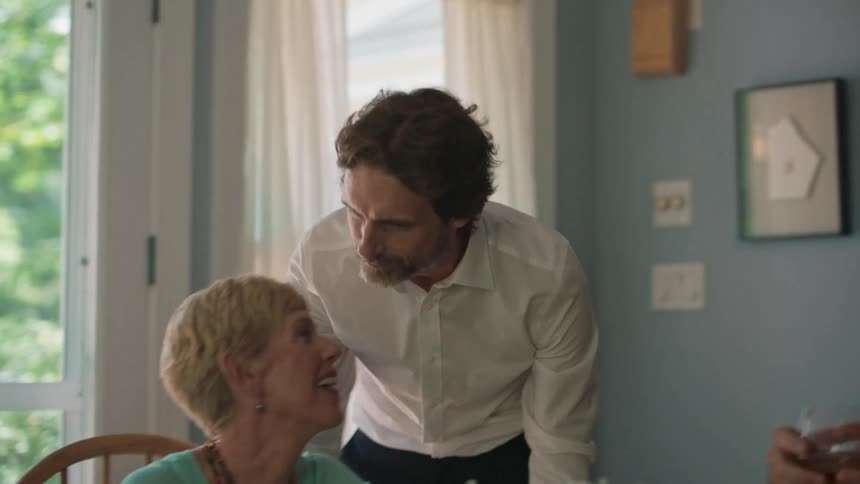 A man kissing an older woman on the forehead as she sits at a dinner table