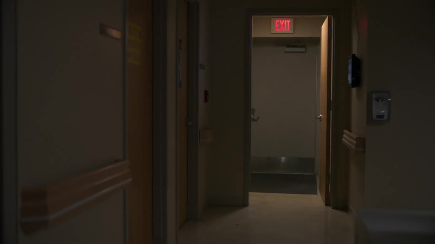 A person in scrubs walks out of a hospital room
