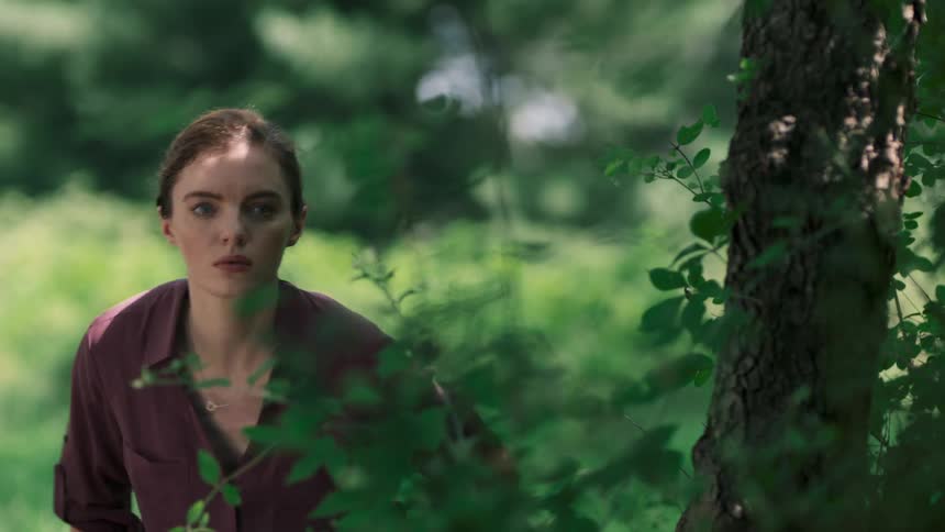 A woman sitting in the grass behind a tree gets up and runs away