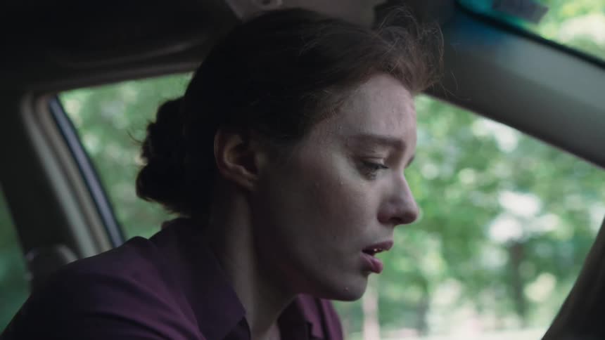 A woman nods her head while sitting in the front seat of her vehicle