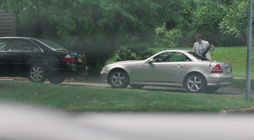 A man places a guitar case in a car then closes the passenger side door