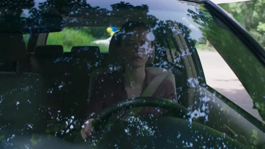 A woman drives a car down a suburban street
