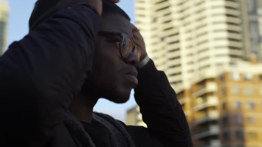 A man who appears upset puts on a knit cap and looks out at the city
