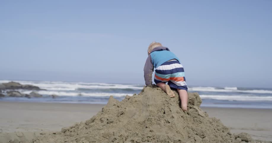 A young boy jumps from a small pile of sand on a beach