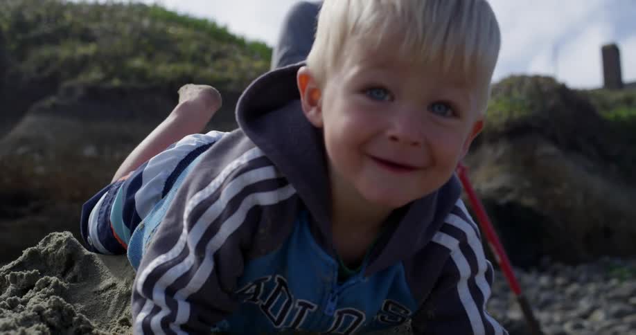 A toddler plays in and crawls through the sand on a beach