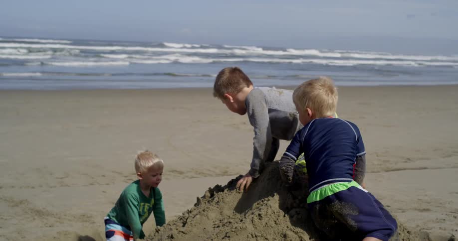 Young boys climb and roll down a large pile of sand at the beach