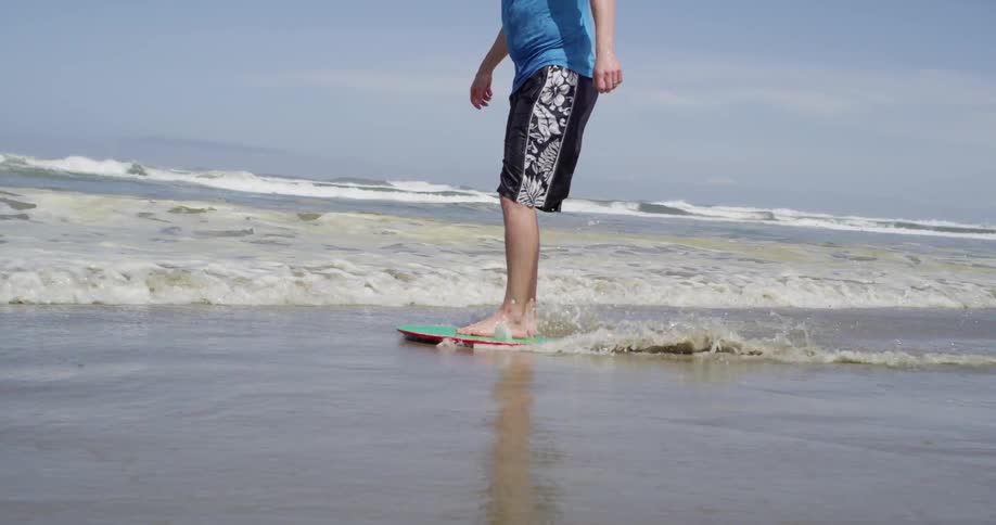 A man runs after a small board and rides it into the ocean
