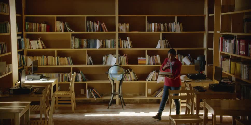 Woman removes a book from a bookshelf and takes a few steps as she opens it