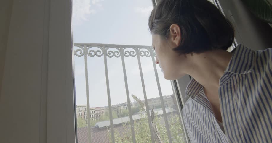 A male teenager stands and looks out the window