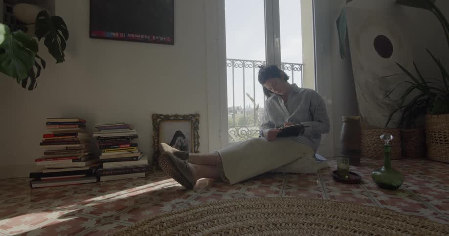 A woman sits on the floor and writes in a book