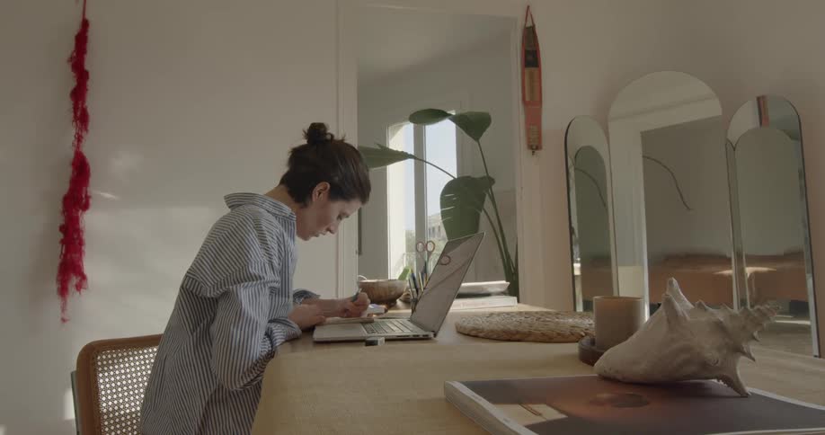 Woman taking notes from laptop while sitting at table indoors
