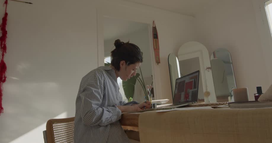A young white woman writes down information taken from her laptop