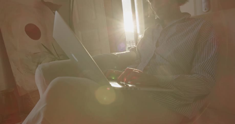 A teenager sits on the couch and uses a laptop