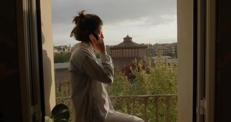 A woman stands on a small balcony talking on the phone