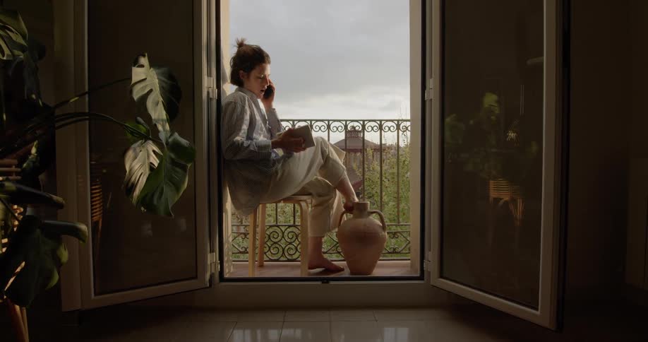 A woman talks on a cell phone while sitting on a chair on a balcony