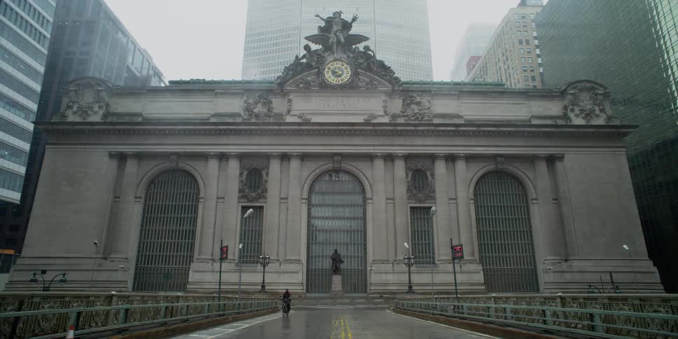 A person riding a bike on the street with a building and skyscrapers in the background