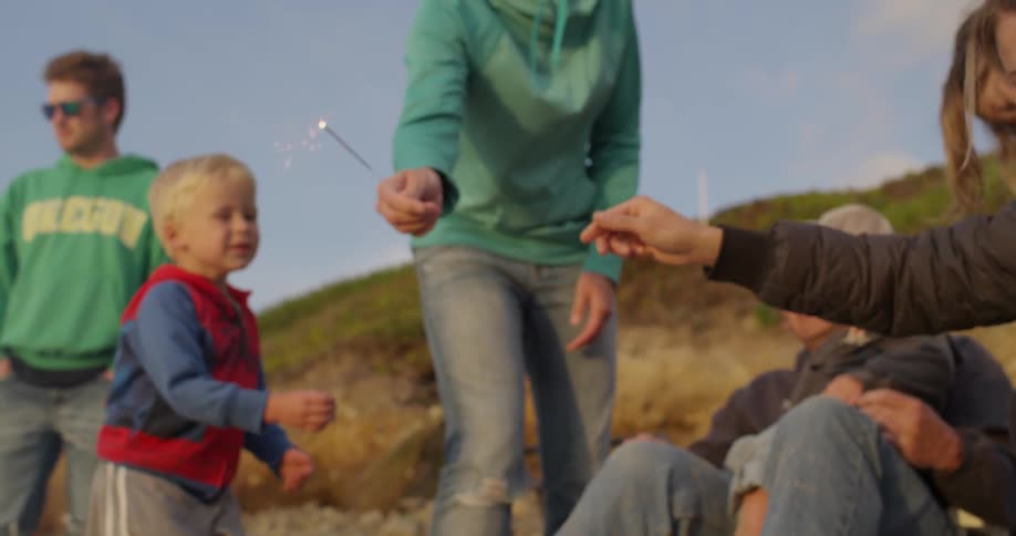 People hand a young boy a sparkler on the beach